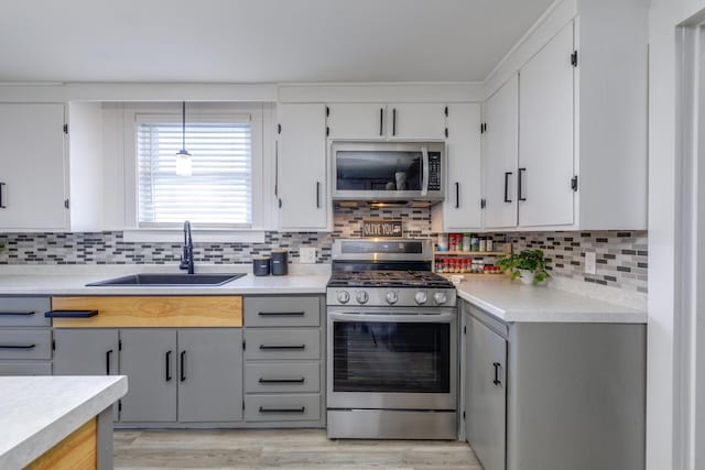 kitchen featuring stainless steel appliances, a sink, light countertops, light wood finished floors, and tasteful backsplash