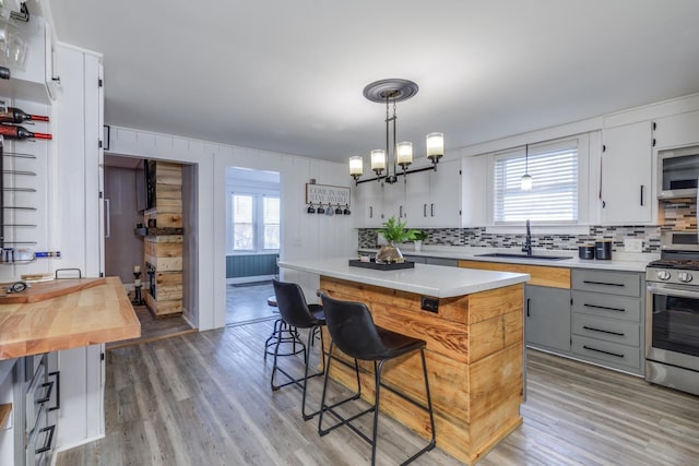 kitchen featuring a sink, backsplash, light wood-type flooring, and stainless steel range with gas cooktop