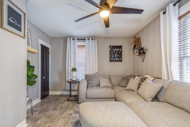 living room with ceiling fan, crown molding, baseboards, and light wood-style floors