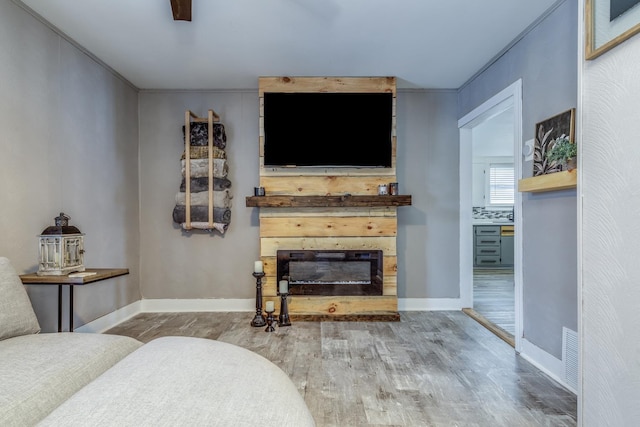 living room featuring wood finished floors, visible vents, baseboards, a glass covered fireplace, and crown molding