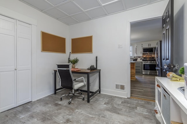 office area with light wood-style floors, visible vents, and baseboards