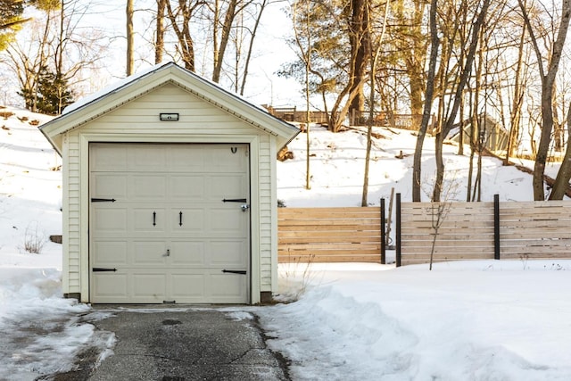 snow covered garage with a detached garage and fence