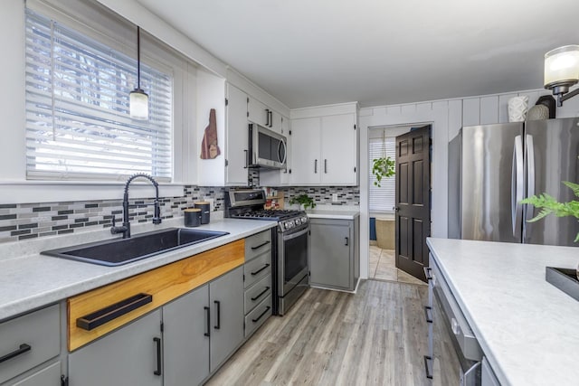 kitchen featuring light countertops, gray cabinetry, decorative backsplash, appliances with stainless steel finishes, and a sink