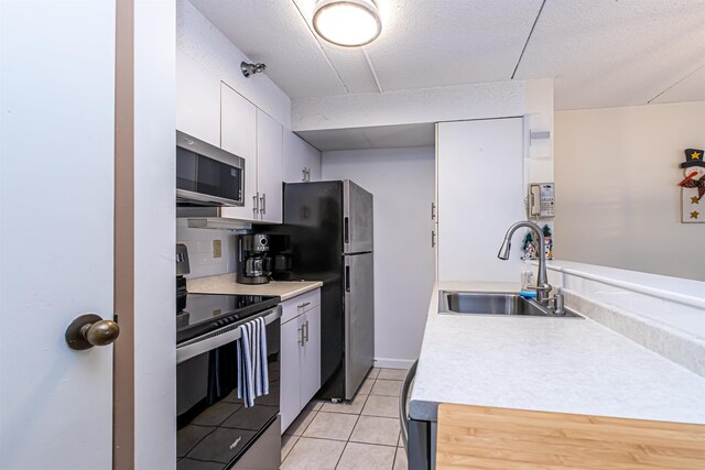 kitchen with stainless steel appliances, light tile patterned flooring, a sink, and light countertops