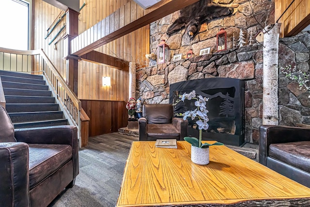 carpeted living room featuring a high ceiling, stairway, a fireplace, and wooden walls