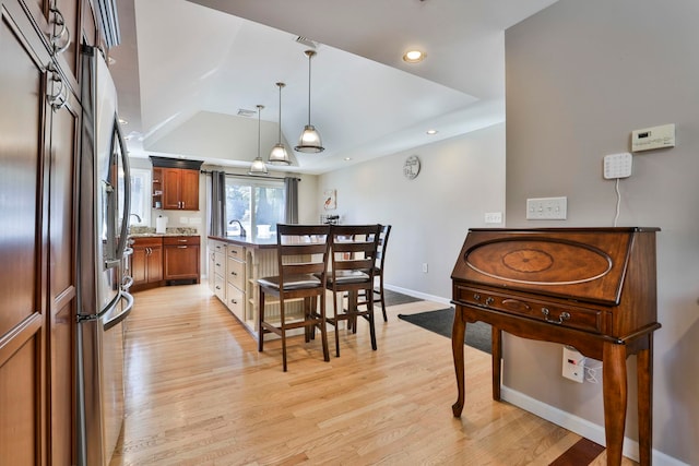 kitchen with a tray ceiling, recessed lighting, light wood-style flooring, stainless steel fridge, and baseboards