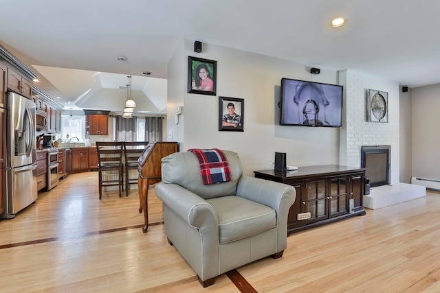 living room with light wood finished floors, recessed lighting, a baseboard radiator, a brick fireplace, and vaulted ceiling