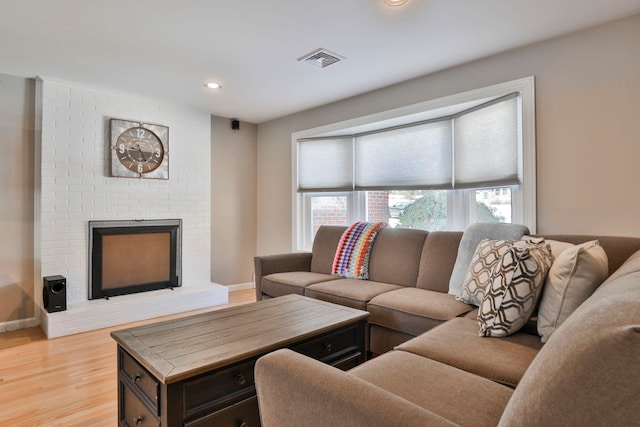 living area with light wood finished floors, a brick fireplace, visible vents, and baseboards