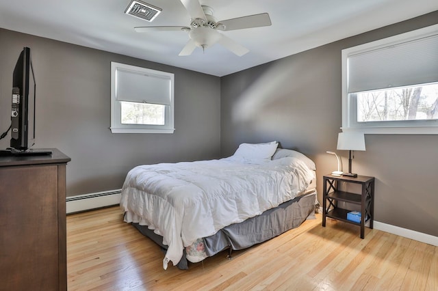 bedroom featuring visible vents, a baseboard heating unit, ceiling fan, wood finished floors, and baseboards