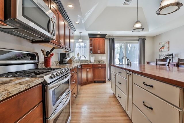 kitchen with appliances with stainless steel finishes, a tray ceiling, pendant lighting, and visible vents