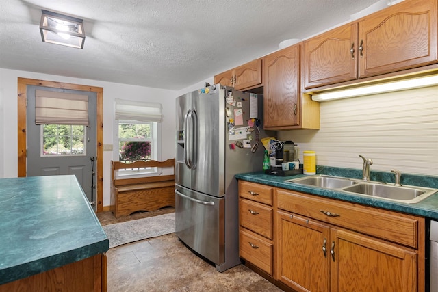 kitchen featuring dark countertops, a textured ceiling, stainless steel refrigerator with ice dispenser, and a sink