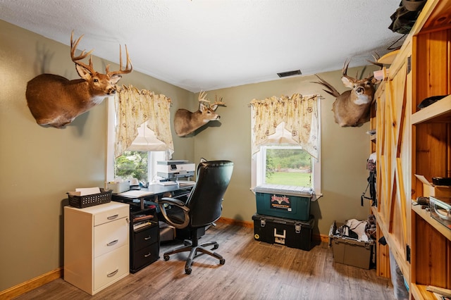 office area with light wood-style floors, baseboards, visible vents, and a textured ceiling