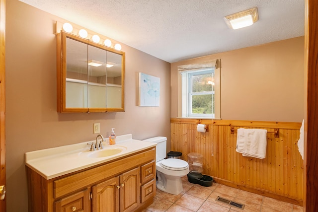 bathroom featuring a textured ceiling, toilet, wooden walls, vanity, and visible vents