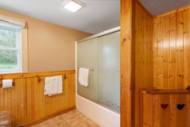 full bathroom with wainscoting, combined bath / shower with glass door, wood walls, a textured ceiling, and tile patterned floors