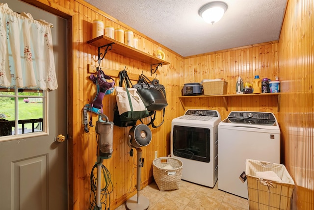 clothes washing area with laundry area, wood walls, a textured ceiling, and separate washer and dryer