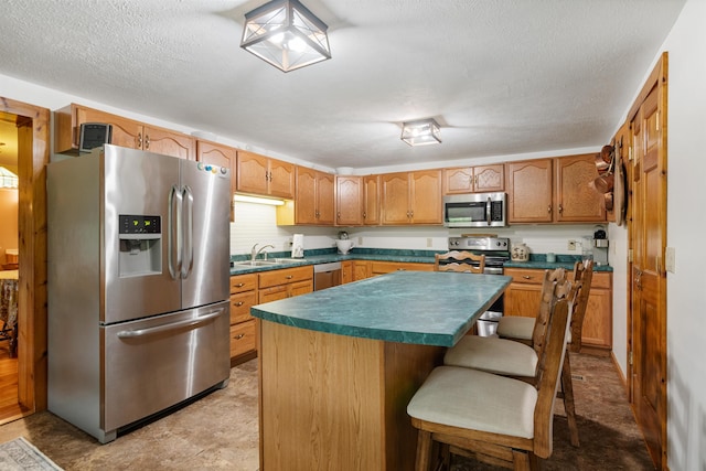 kitchen with dark countertops, a kitchen island, stainless steel appliances, a textured ceiling, and a sink