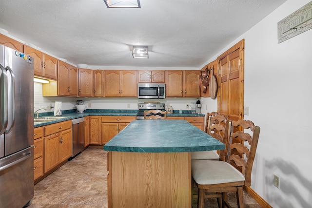 kitchen with a breakfast bar, stainless steel appliances, dark countertops, a kitchen island, and a sink