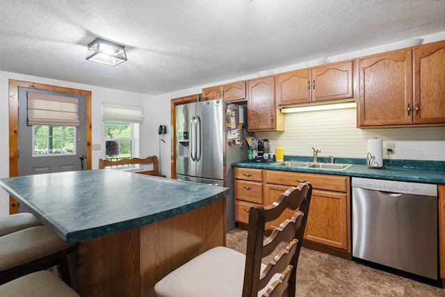 kitchen with a textured ceiling, a breakfast bar area, a sink, appliances with stainless steel finishes, and dark countertops