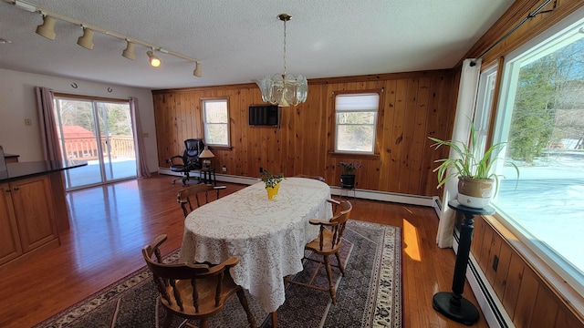 dining room with wood walls, a textured ceiling, a baseboard heating unit, and wood finished floors