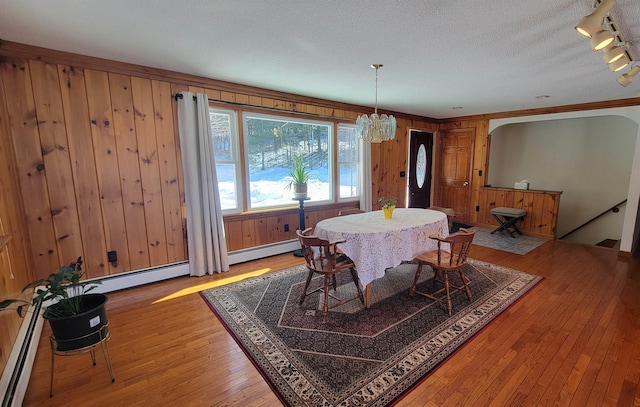 dining area with wooden walls, a baseboard radiator, a textured ceiling, and hardwood / wood-style flooring