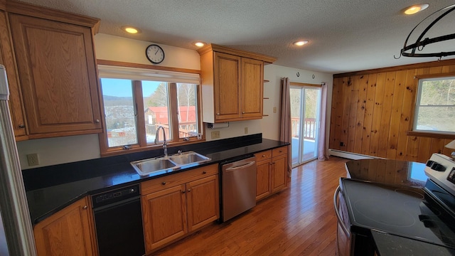 kitchen with a baseboard radiator, a sink, appliances with stainless steel finishes, brown cabinetry, and dark countertops