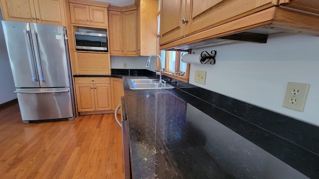 kitchen with stainless steel appliances, light wood-style floors, a sink, and dark stone countertops