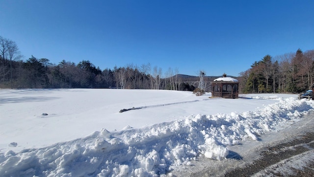 yard covered in snow with a wooded view and a gazebo