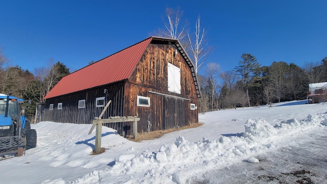 view of snowy exterior featuring a barn, a gambrel roof, a detached garage, metal roof, and an outdoor structure