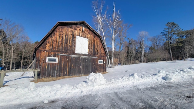 view of snowy exterior with an outbuilding, a detached garage, a barn, and a gambrel roof