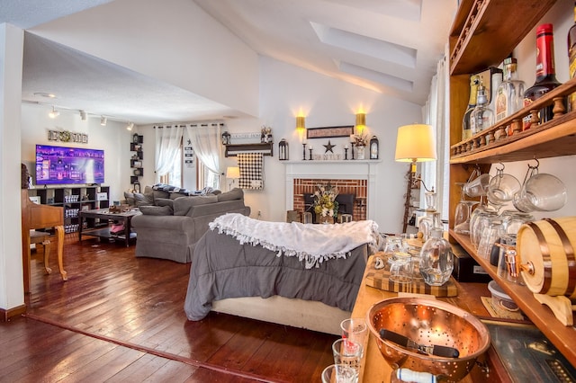 living area with lofted ceiling, rail lighting, a fireplace, and hardwood / wood-style floors