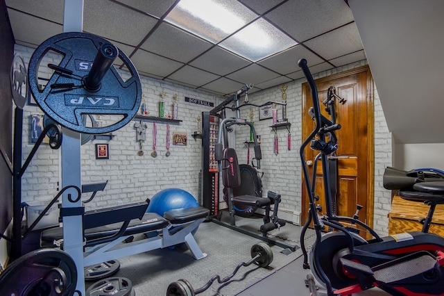 exercise area featuring a paneled ceiling and brick wall