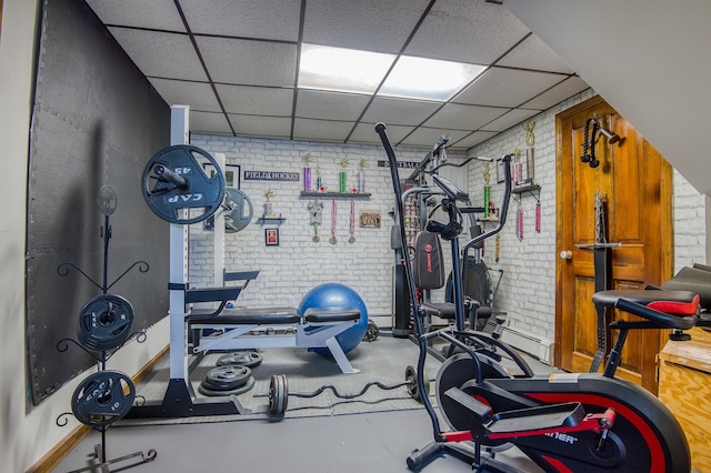 exercise room with brick wall and a drop ceiling