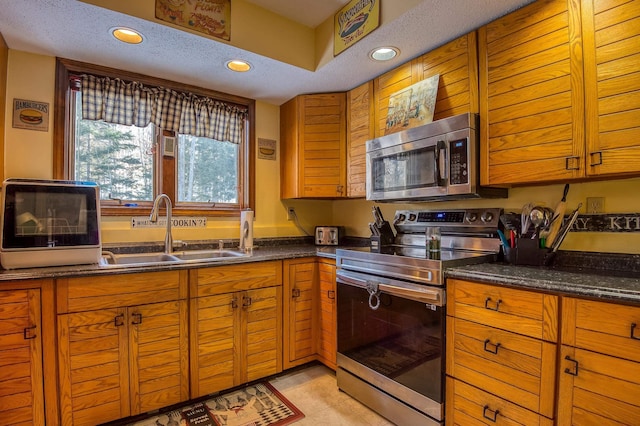 kitchen featuring brown cabinets, recessed lighting, appliances with stainless steel finishes, a sink, and dark stone counters