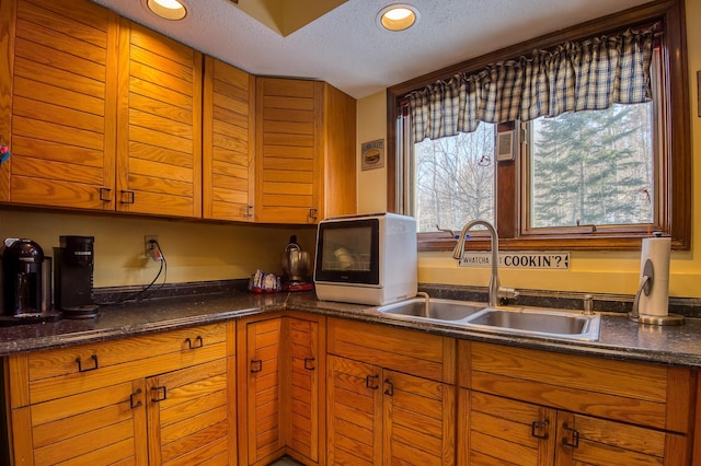 kitchen featuring brown cabinets, a healthy amount of sunlight, a sink, and a textured ceiling