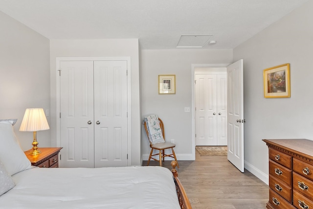 bedroom with light wood-style floors, attic access, baseboards, and a closet