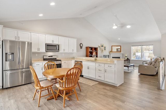 kitchen featuring appliances with stainless steel finishes, open floor plan, a peninsula, light countertops, and a sink