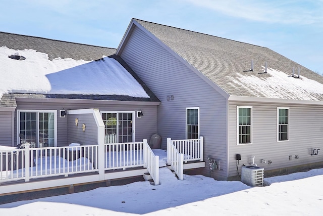 snow covered rear of property featuring a shingled roof, a deck, and central AC