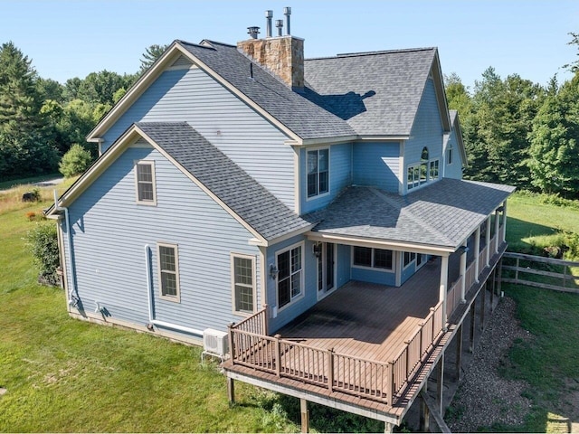 back of house featuring a shingled roof, a chimney, a deck, and a lawn