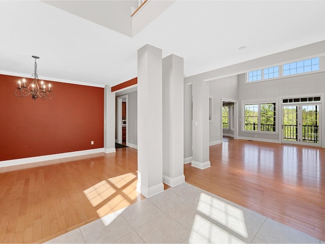 unfurnished room with a notable chandelier, a towering ceiling, baseboards, and wood finished floors