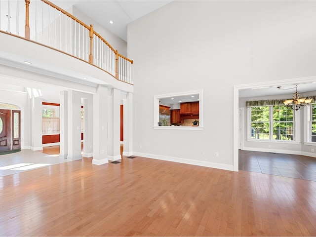 unfurnished living room with baseboards, hardwood / wood-style floors, a towering ceiling, and an inviting chandelier