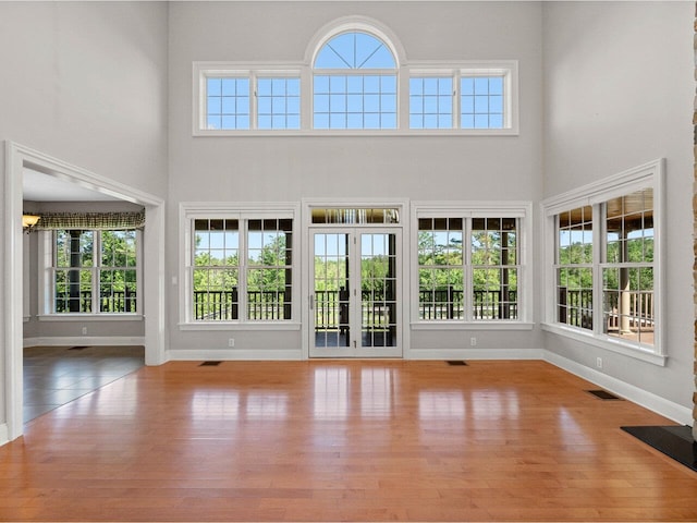 interior space featuring a towering ceiling, baseboards, visible vents, and wood finished floors