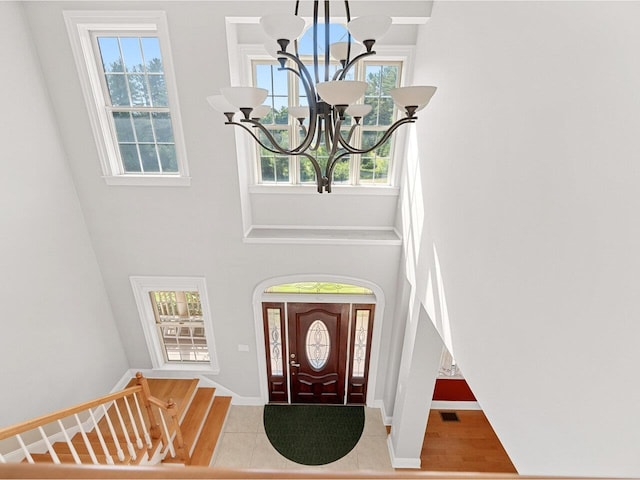 entrance foyer with visible vents, a notable chandelier, a towering ceiling, and baseboards