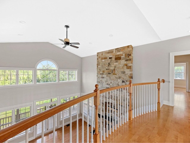 corridor with high vaulted ceiling, wood finished floors, an upstairs landing, and baseboards