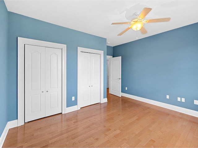 unfurnished bedroom with multiple closets, baseboards, light wood finished floors, and a ceiling fan