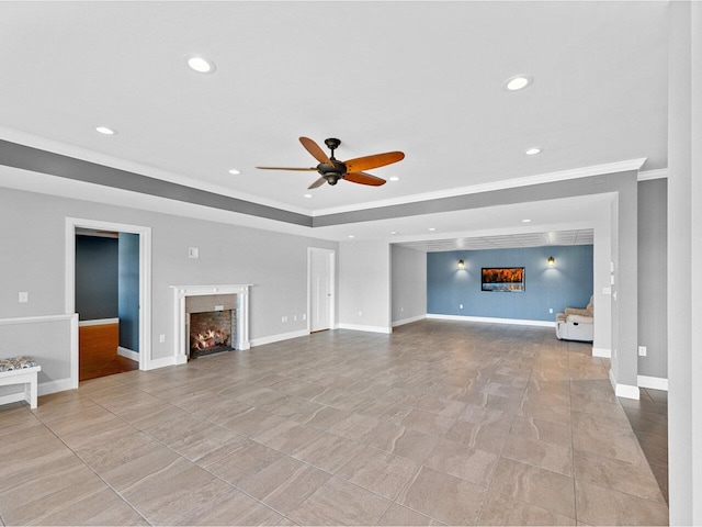 unfurnished living room featuring recessed lighting, a warm lit fireplace, a tray ceiling, and baseboards