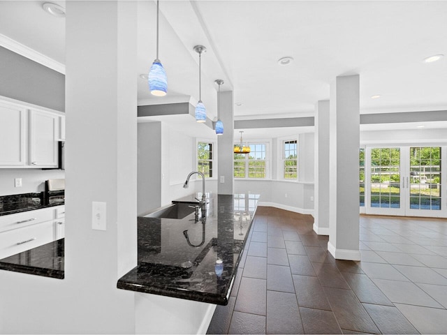 kitchen with baseboards, dark stone counters, white cabinets, pendant lighting, and a sink