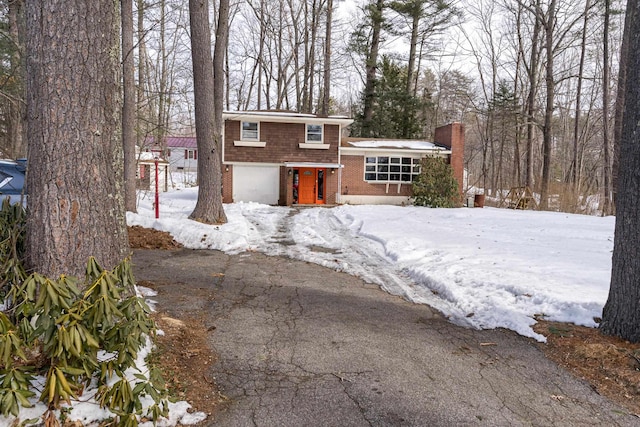 tri-level home featuring a garage, brick siding, driveway, and a chimney