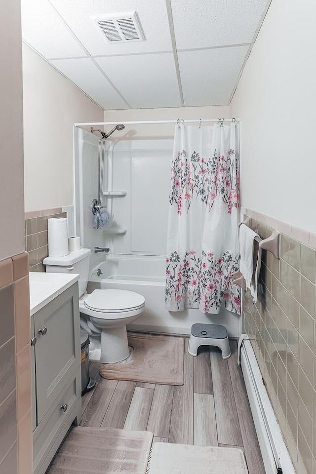 bathroom featuring visible vents, wood finished floors, baseboard heating, shower / bath combination with curtain, and tile walls