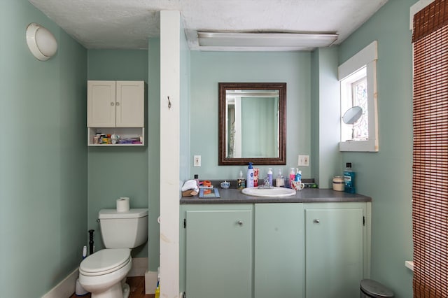 bathroom with a textured ceiling, vanity, toilet, and baseboards