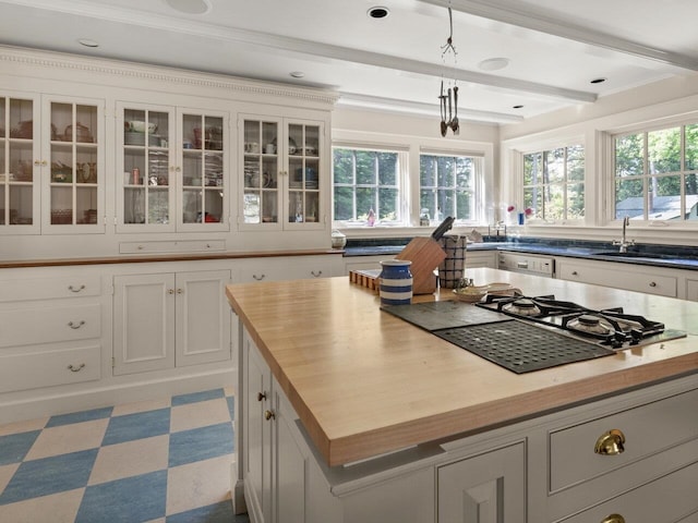 kitchen featuring glass insert cabinets, beamed ceiling, a sink, pendant lighting, and wooden counters